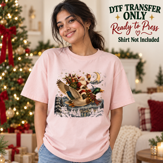 Model wearing a pink shirt showing Santa riding a flying duck over a snowy scene; DTF transfer only, shirt not included.
