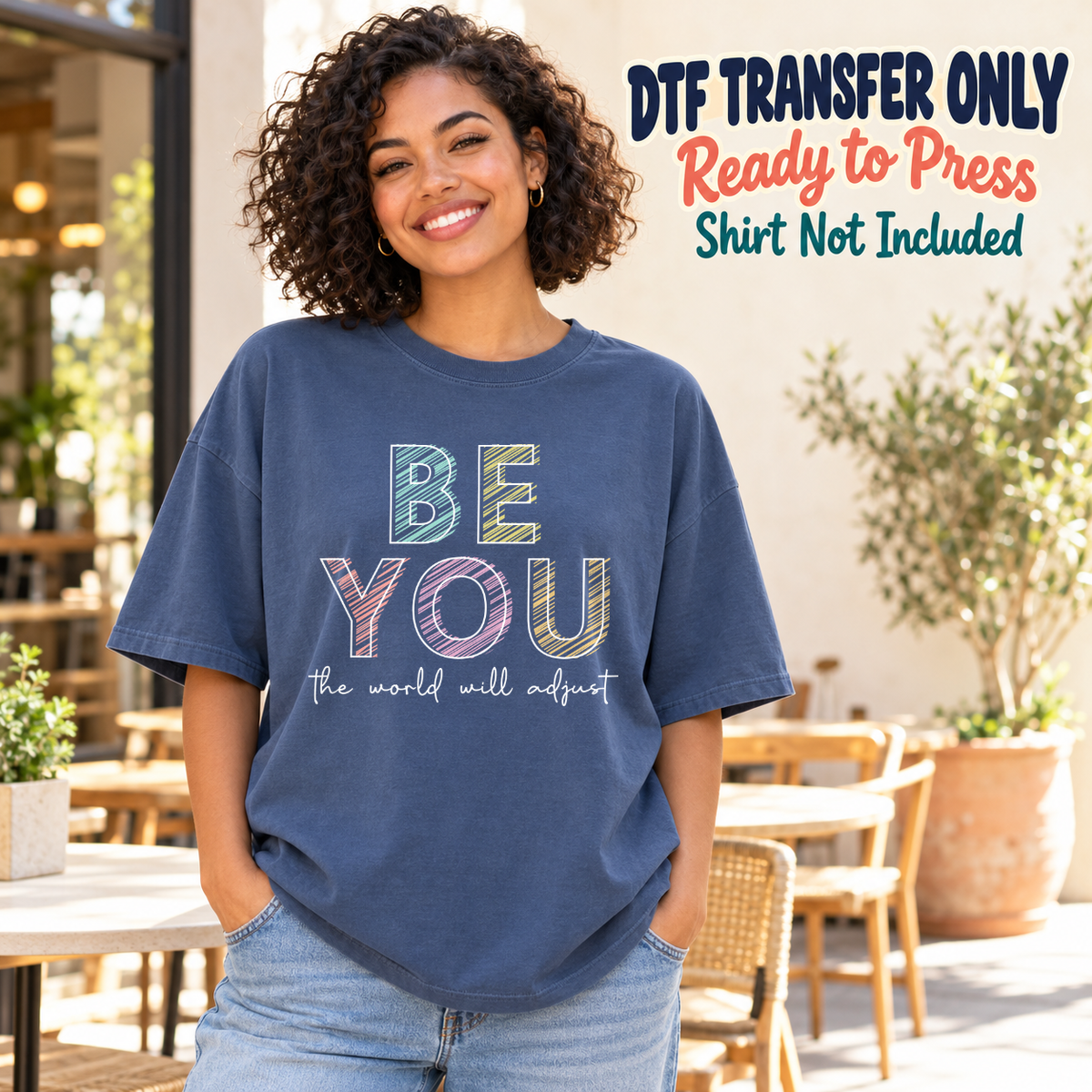 Model wearing a navy shirt showing Be You the World Will Adjust in pastel light-outlined letters; DTF transfer only, shirt not included.