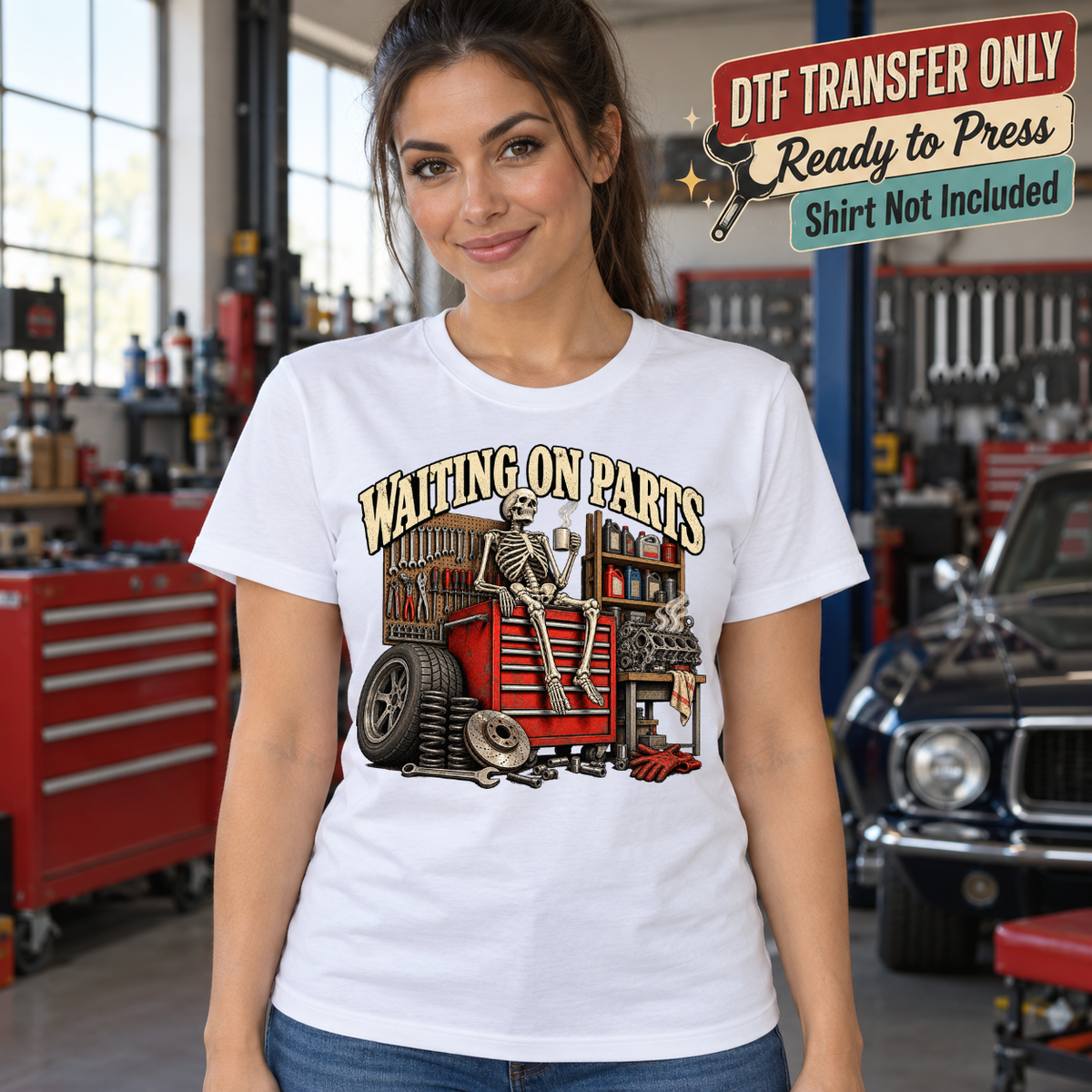 Model wearing a white shirt with waiting on parts skeleton at red tool chest with tires; DTF transfer only, shirt not included.