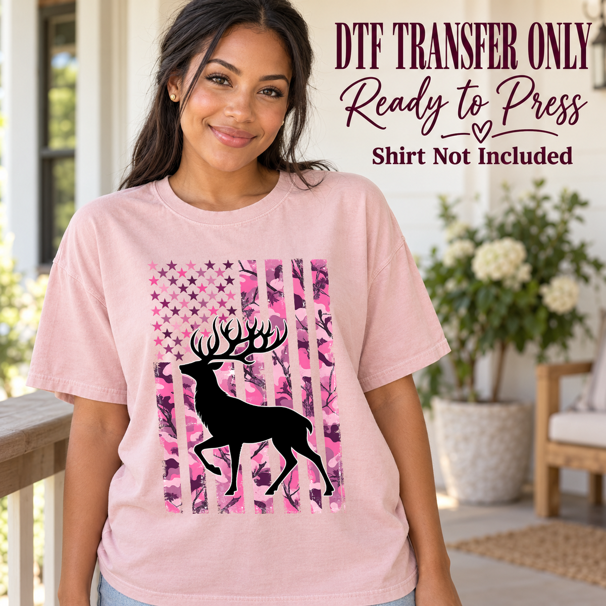 Deer silhouette over a pink camouflage American flag shown on a pink shirt worn by a woman; DTF transfer only, shirt not included.