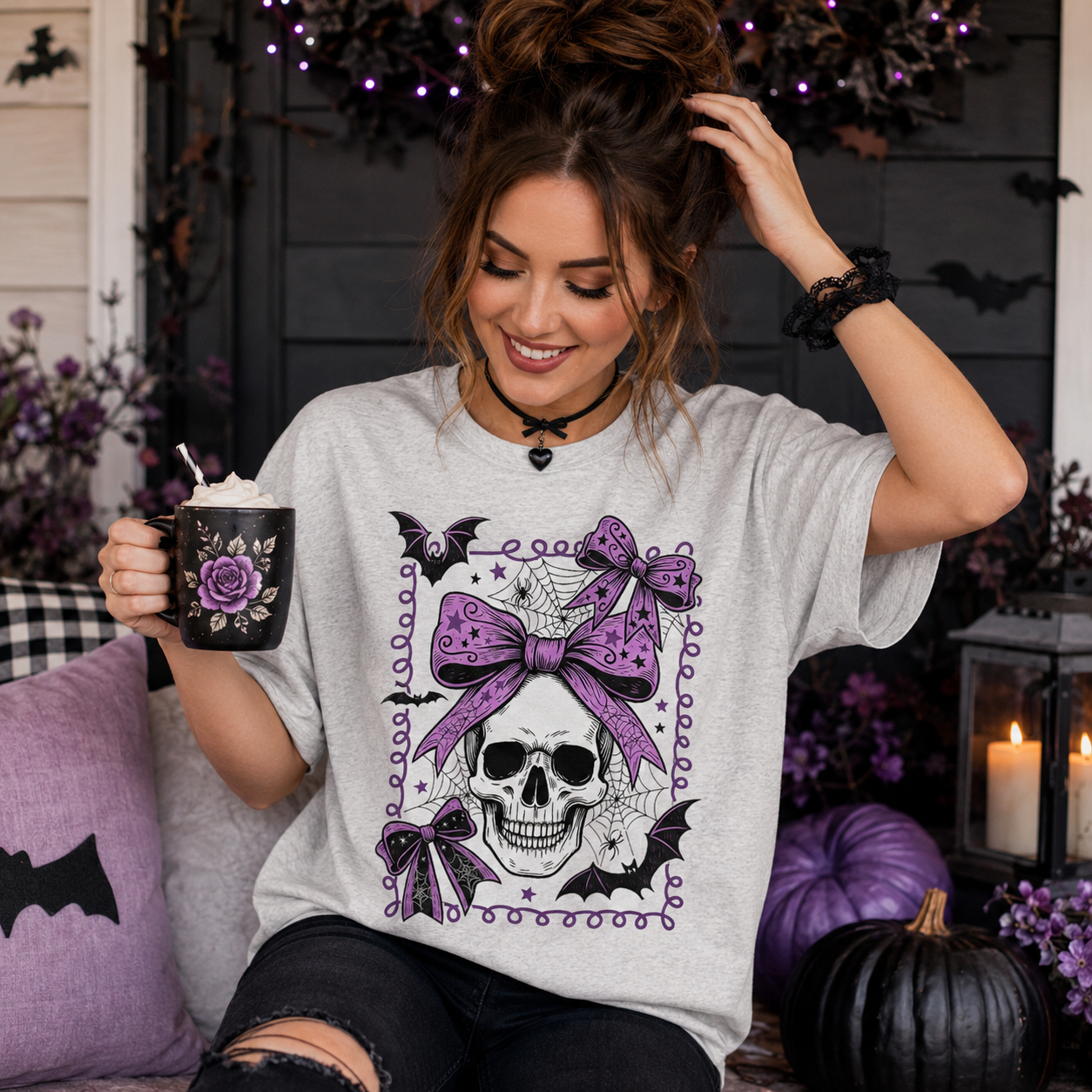 A woman wearing a light gray t-shirt with a purple and black gothic skull graphic, holding a mug in a decorated Halloween setting.