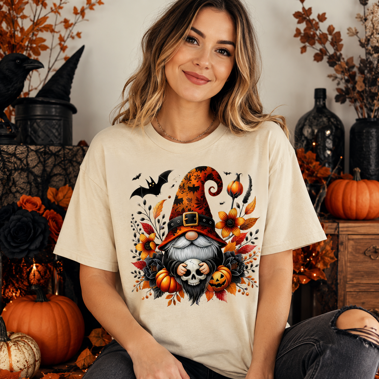 A woman wearing a cream-colored graphic t-shirt with a Halloween gnome design, posed in a cozy autumn-themed setting with pumpkins and fall decorations.