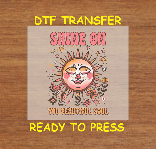 "DTF transfer featuring a smiling sun with flowers and the phrase 'Shine On You Beautiful Soul' in vibrant colors."