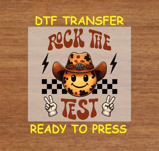 Rock the Test DTF transfer with cow print smiley, cowboy hat, peace signs, checkered pattern, and lightning bolts.
