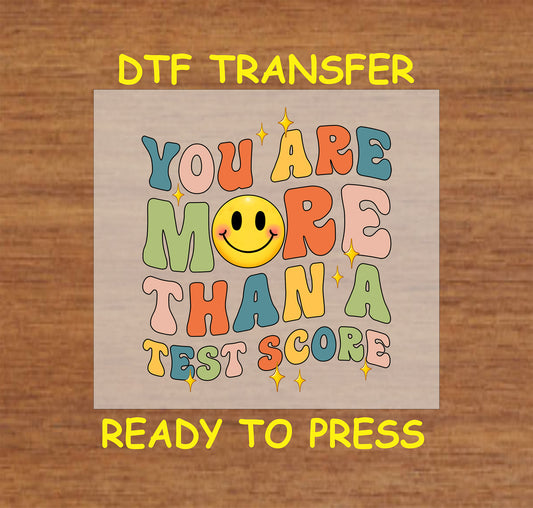 Retro-style "More Than a Test Score" DTF transfer with colorful text and a smiley face.