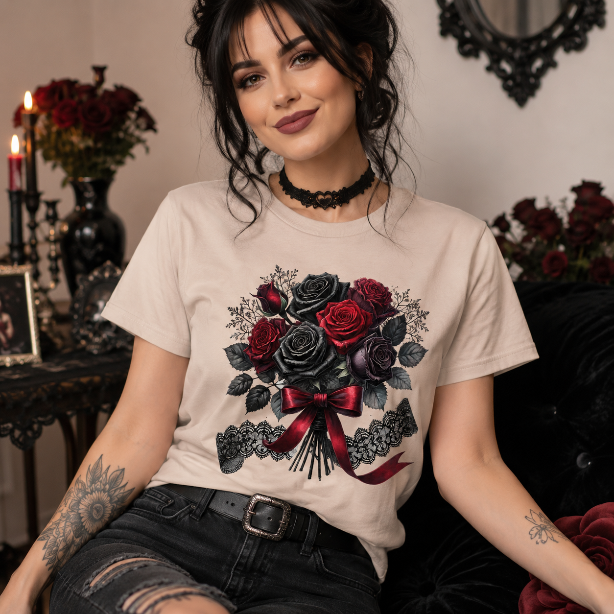 A woman wearing a beige graphic t-shirt with a black and red rose design, paired with distressed black jeans, sitting in a gothic-themed room with candles and dark floral arrangements.