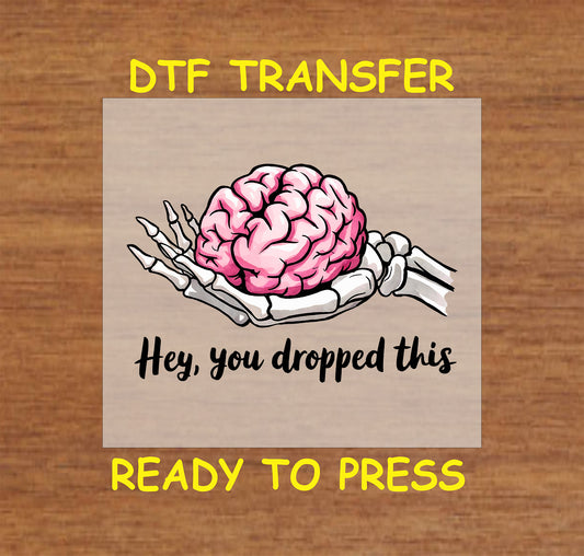 DTF transfer with skeleton hand holding pink brain and text saying Hey, you dropped this.