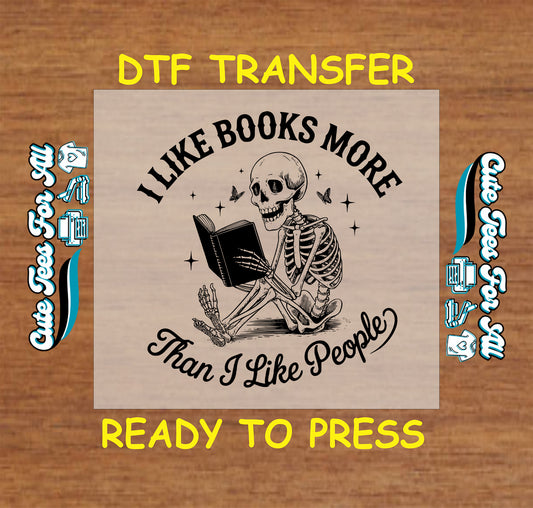 Black and white DTF transfer of a skeleton reading a book with the quote “I Like Books More Than I Like People”