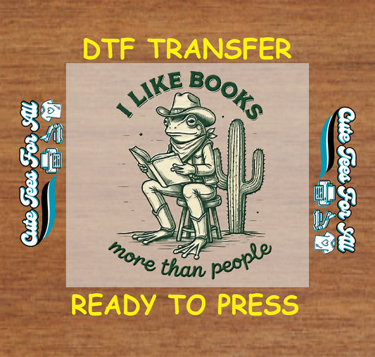 Cowboy frog reading a book with cactus and text “I Like Books More Than People” on a DTF transfer.