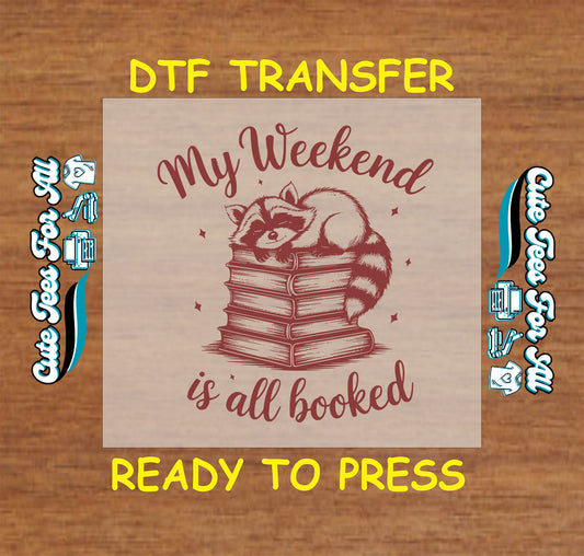 DTF transfer with raccoon laying on stacked books and text “My Weekend Is All Booked”