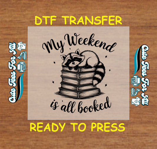 Black and white DTF transfer with raccoon laying on stacked books and text “My Weekend Is All Booked”
