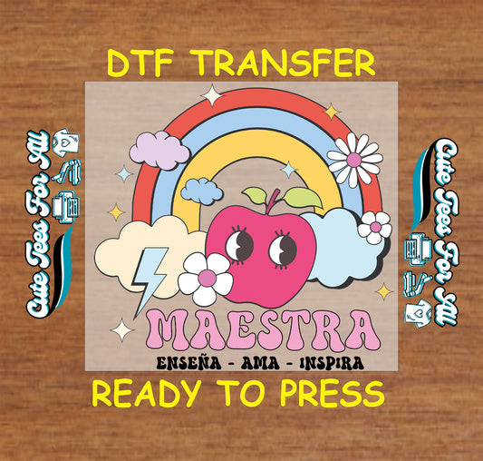 DTF transfer with pastel rainbow, apple, clouds, and the word "Maestra" in bold pink letters with "Enseña Ama Inspira" underneath.