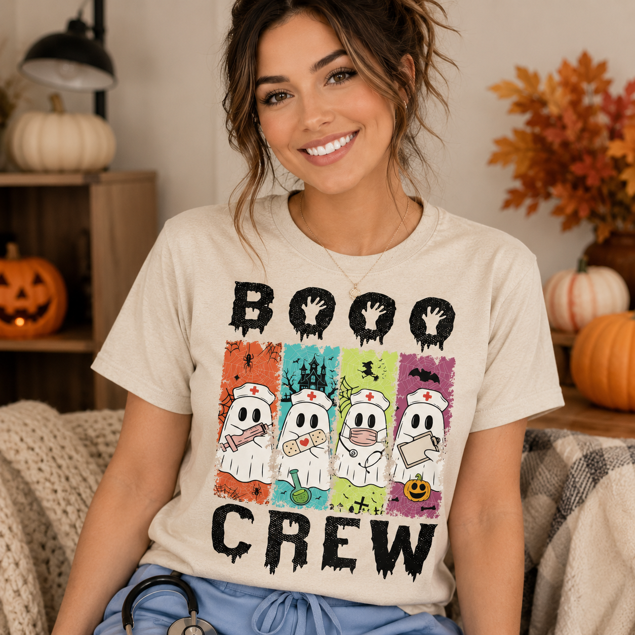 A woman wearing a cream-colored graphic t-shirt with a 'BOOHOO CREW' Halloween print, sitting in a cozy, autumn-themed room with pumpkins and fall decor.