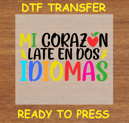 Mi Corazón Late en Dos Idiomas' DTF Transfer design with colorful text and an apple graphic, celebrating bilingualism. Ready to press